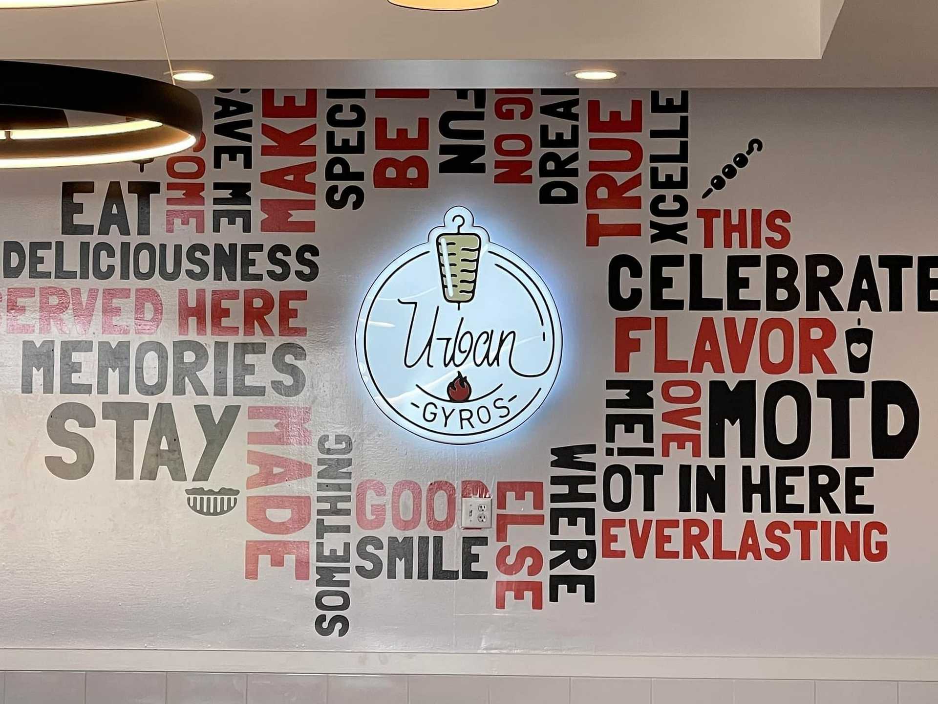 Restaurant wall with Urban Gyros logo surrounded by food-related words and phrases in various fonts.