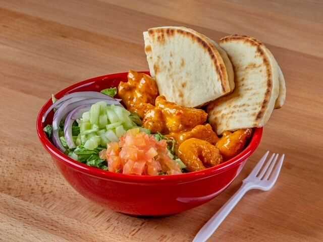 Red bowl with curry chicken, pita bread, diced vegetables, and a white fork on a wooden table.