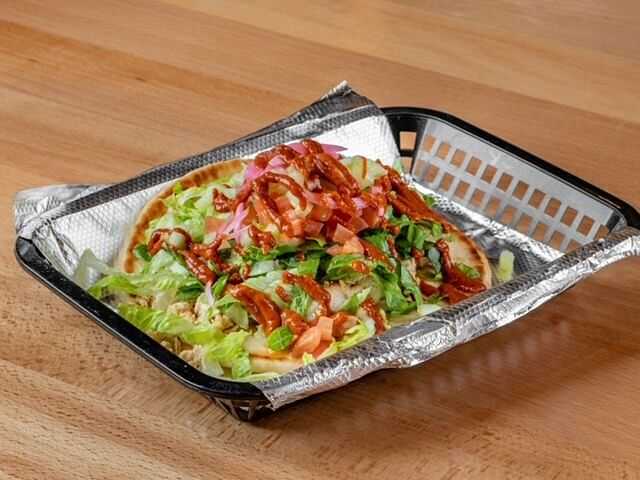 Chicken shawarma wrap with vegetables, drizzled with sauce, served in a basket on foil.