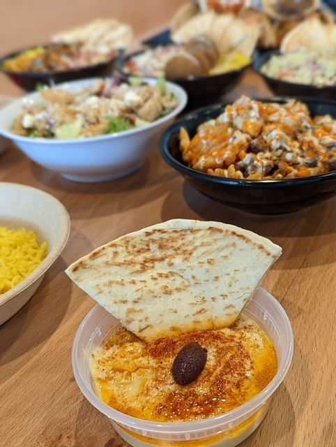 A variety of dishes on a wooden table, featuring hummus topped with a pita slice and olive.