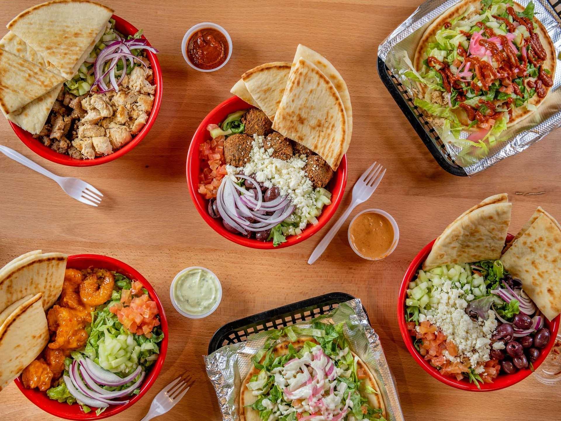 A table with various Mediterranean dishes, including falafel, shrimp, pita, and assorted salads.